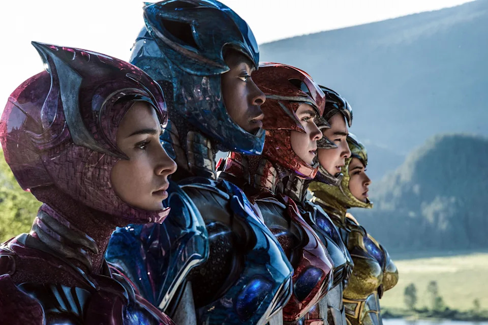 Five people in futuristic armor stand side by side, gazing forward, with mountainous landscape in the background