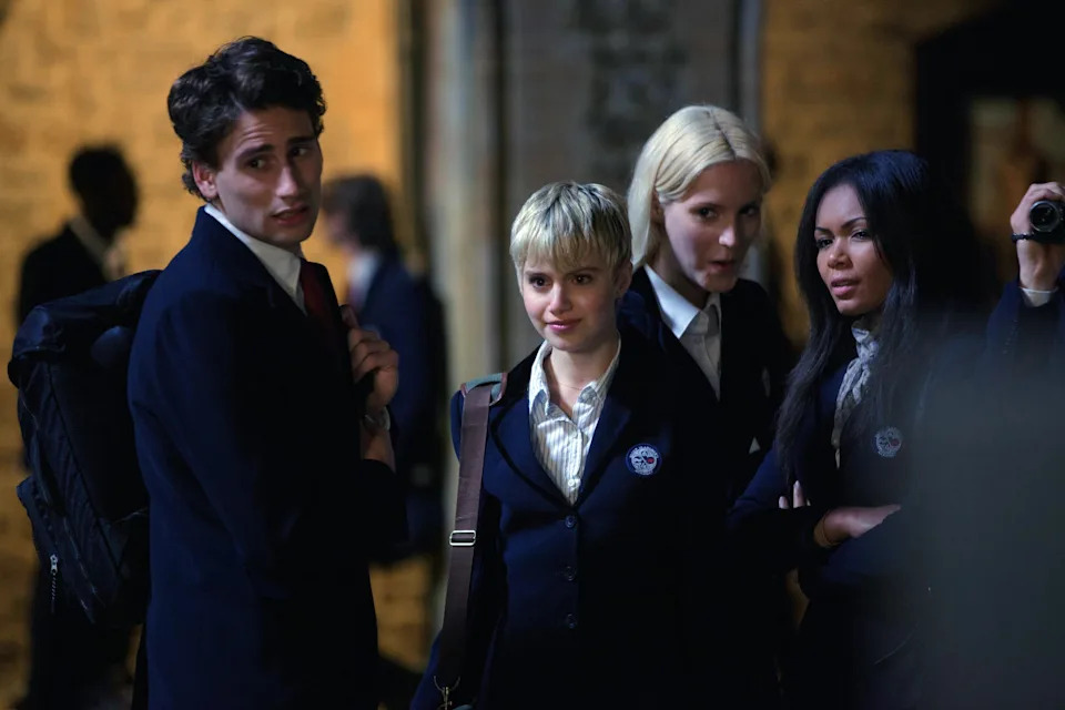 Group of actors in school uniforms, standing together with one holding a camera, possibly a scene from a TV or movie set