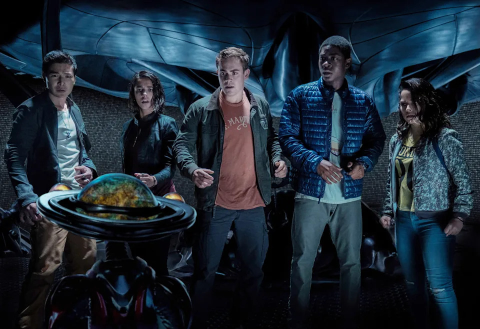 Five people stand in a sci-fi setting, looking intensely at a glowing object with a futuristic backdrop