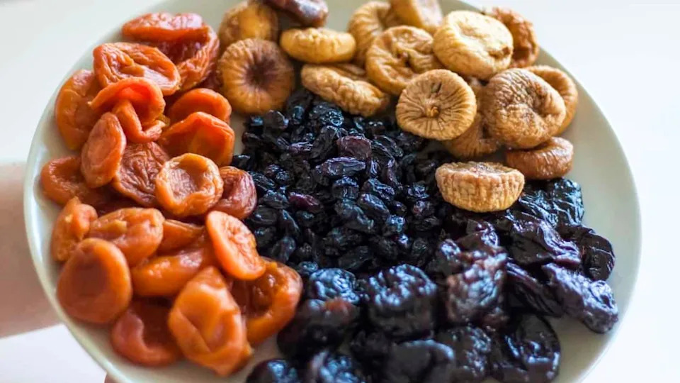 A plate with sections of dried apricots, dried figs, raisins, and dried prunes—healthy foods high in sugar—arranged in groups.