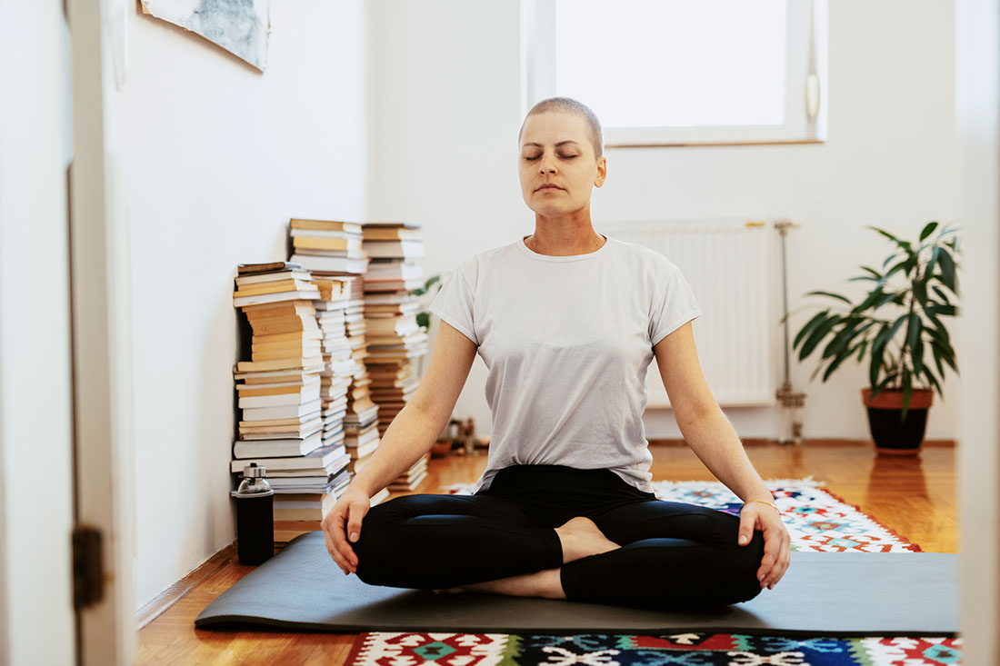 Female wearing a head scarf, doing yoga on a mat in her apartment
