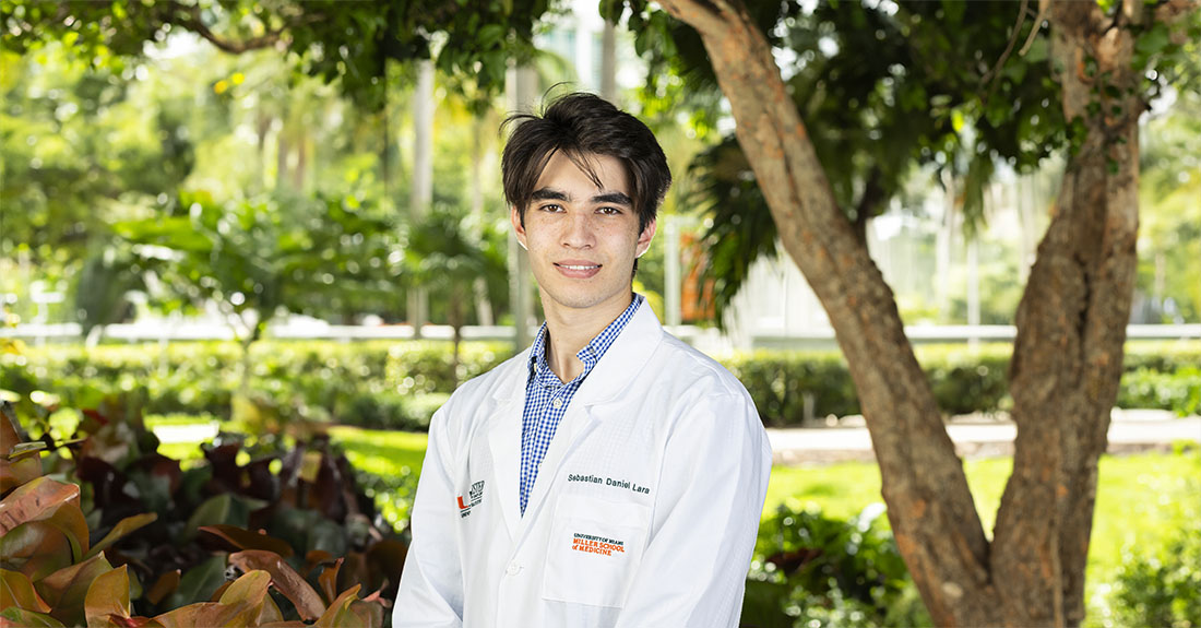 Sebastian Lara, a NEXCITE participant, wears a white University of Miami Miller School of Medicine lab coat outdoors.