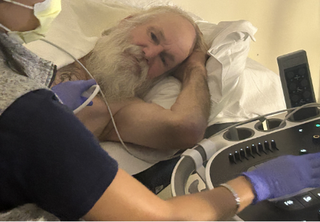 A patient is on an examination bed for an imaging procedure while a clinician operates an ultrasound device to evaluate the heart.