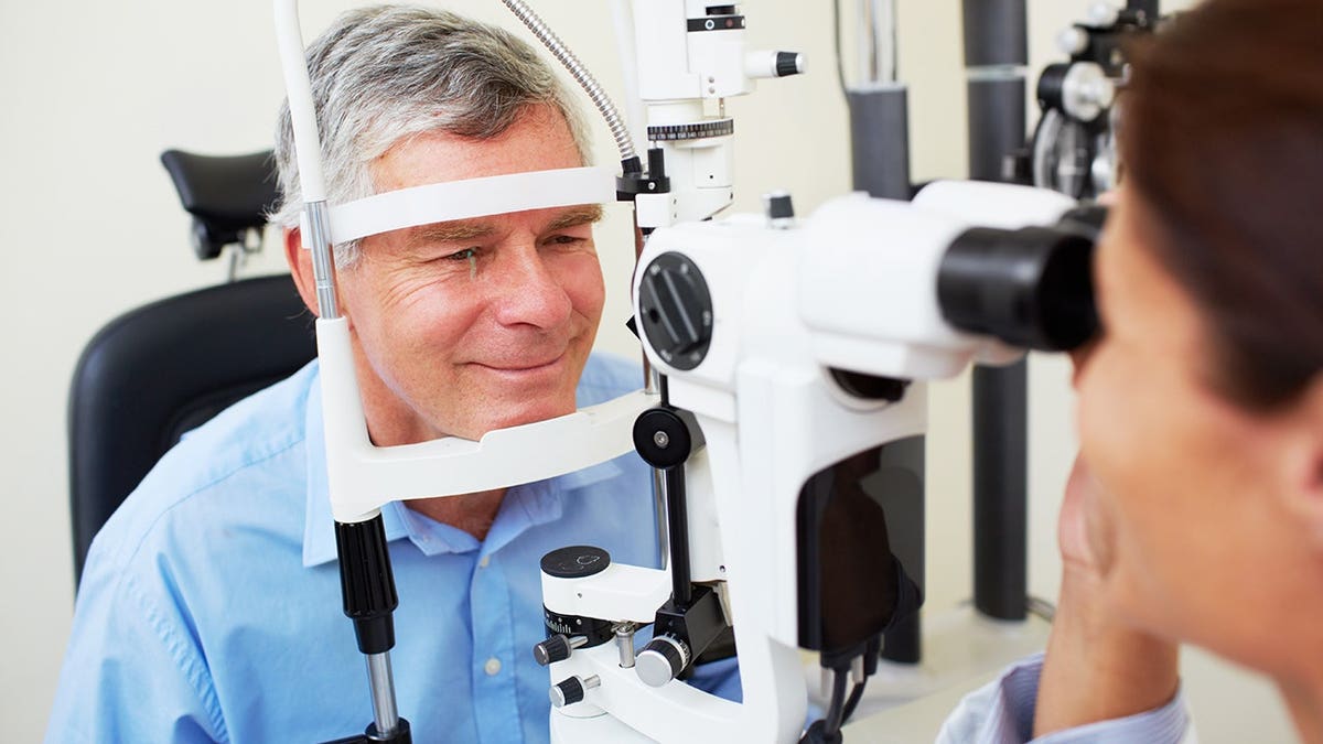 Young optometrist examines patient's eye with slit lamp.