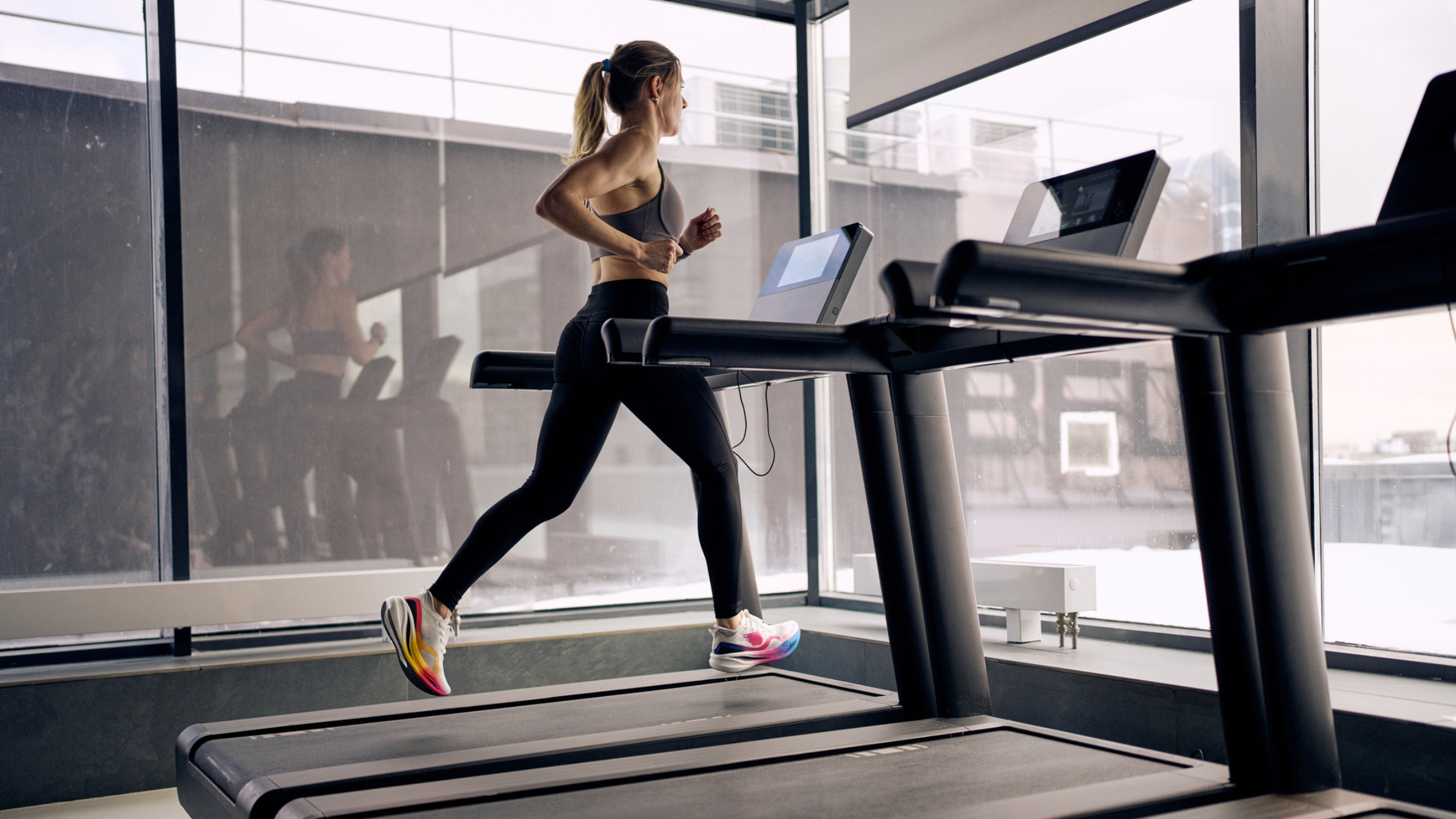 young woman in leggings and sports bra runs on treadmill in modern gym