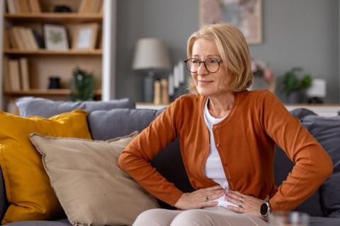 Older woman sitting with hands on lower belly, looking uncomfortable
