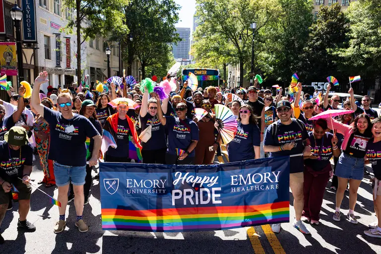 group of people in Emory shirts carrying a Happy Pride banner during a parade