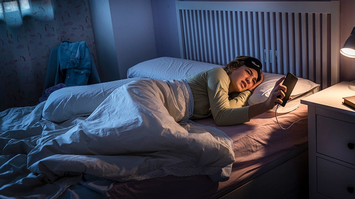 Teenage girl checks smartphone time in bed at night