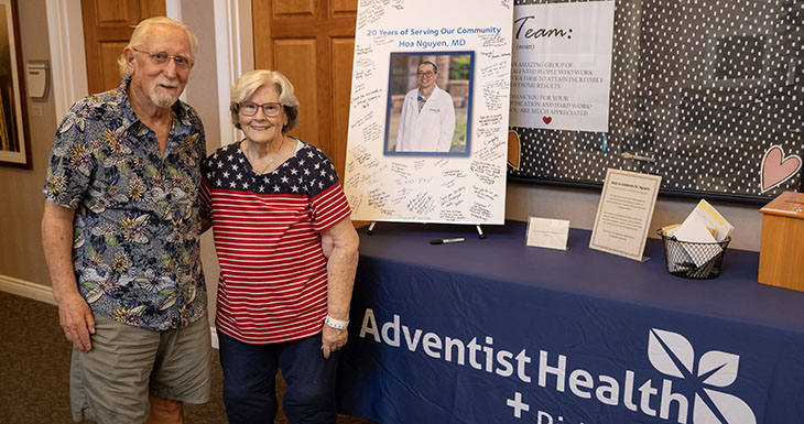 A man and woman stand near a table with an Adventist Health sign and a poster celebrating Dr. Hoa Nguyen's years of service.