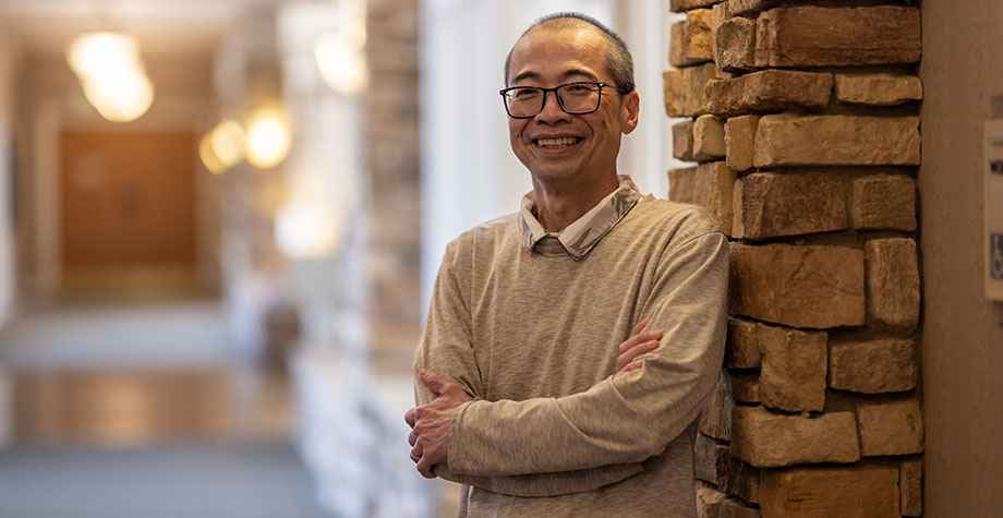 Oncologist Hoa Nguyen, in a tan sweater, smiles while crossing his arms, standing next to a brick column at Rideout Cancer Center.