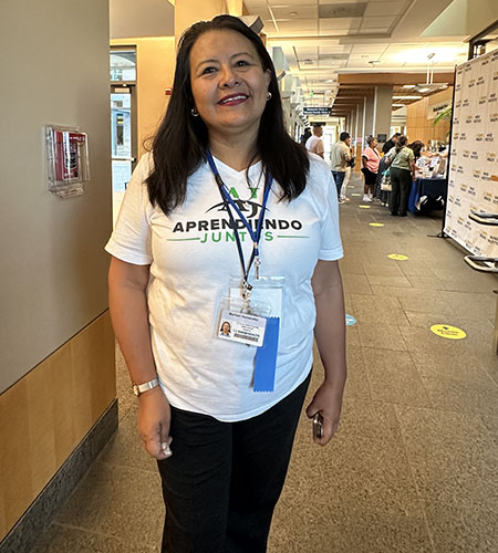 Maribel Hernandez, wearing a white shirt that reads “Aprendiendo Juntos” stands in the MIND Institute lobby.