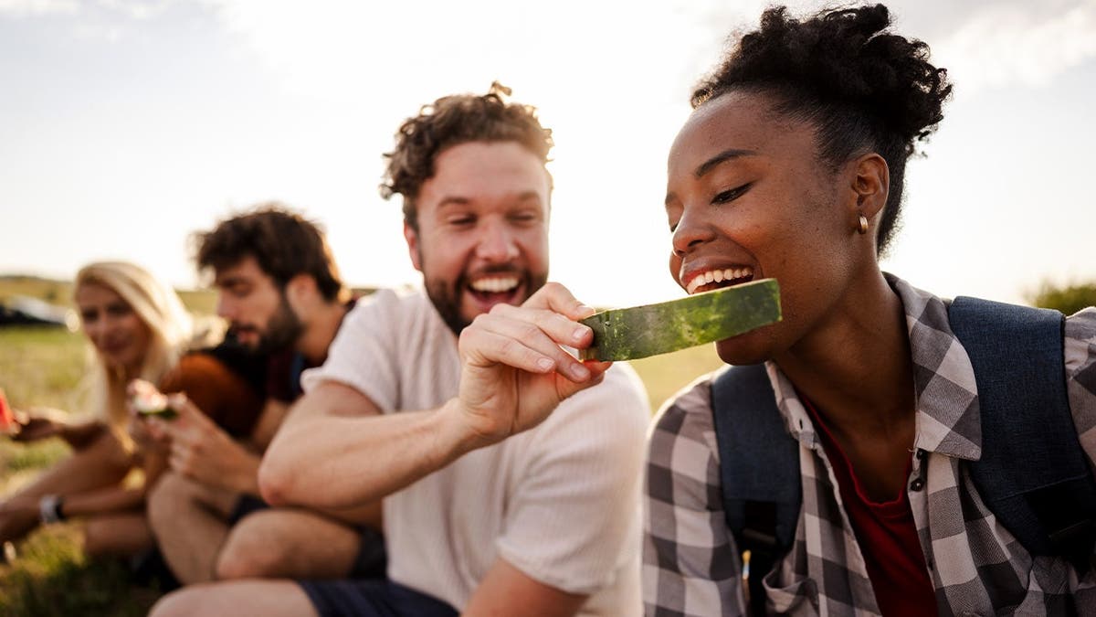 A friend feeds another friend a pice of watermelon.