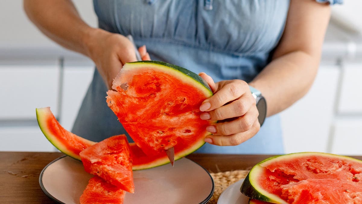 A woman cuts watermelon in her kitchen.