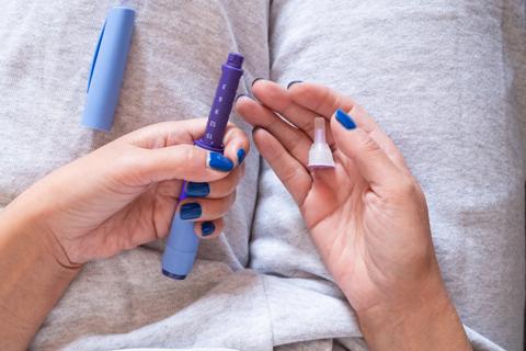 Person holding medication injector in lap with their hands