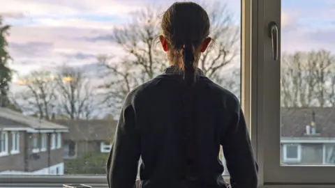 Getty Images A young girl stands at a window and looks out on to a neighbourhood