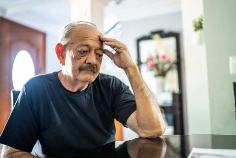 older person, sitting at table with head in hand, looking agitated