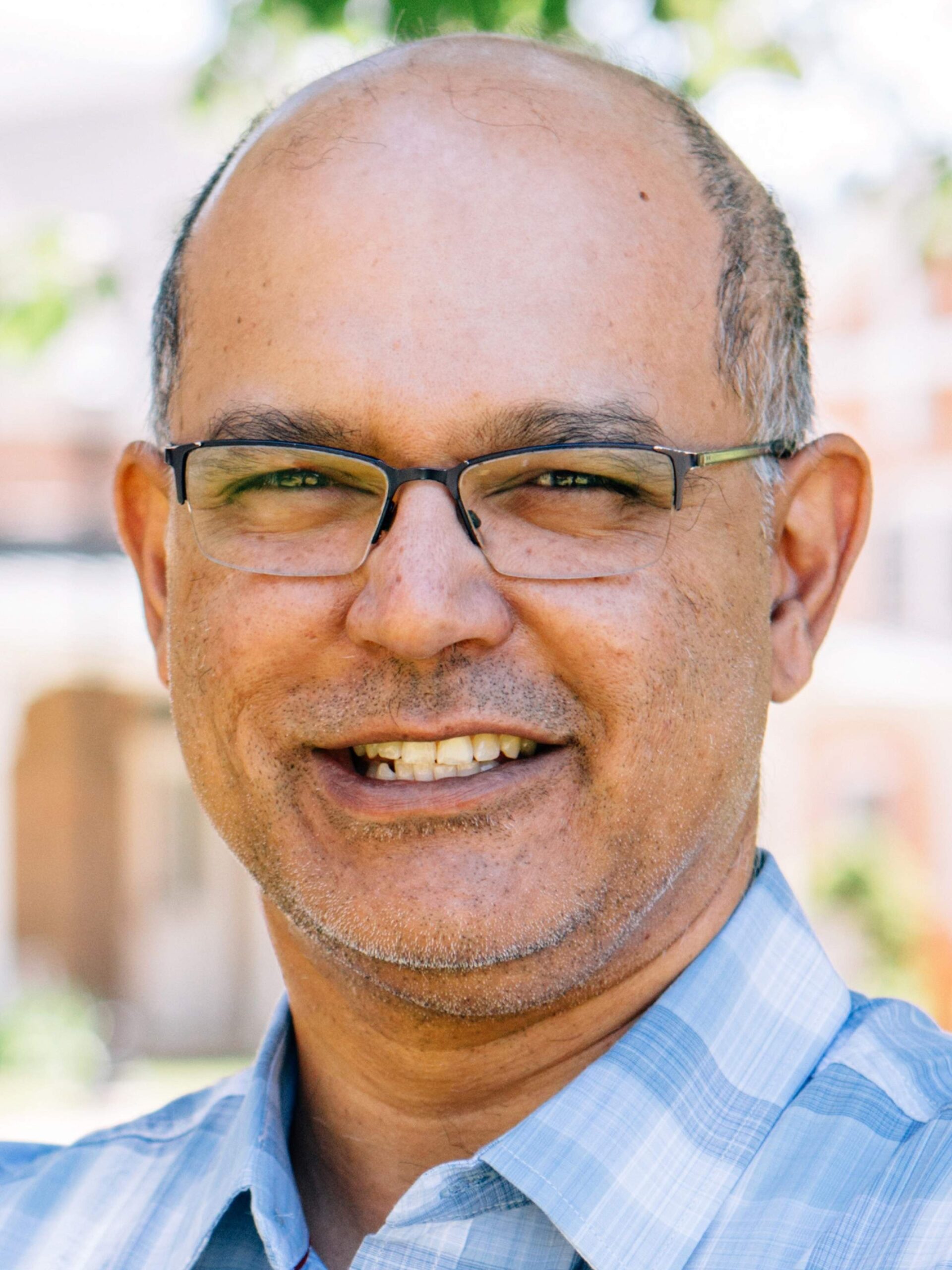 Profile photo of a smiling man in a blue button-up, outside.