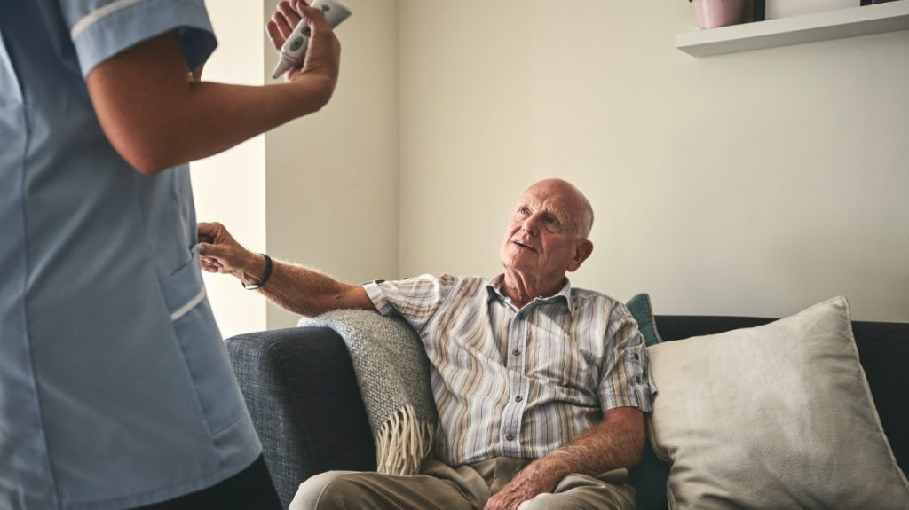 An older adult male listens to a healthcare professional explain the importance of weight management for longevity while sitting on a couch