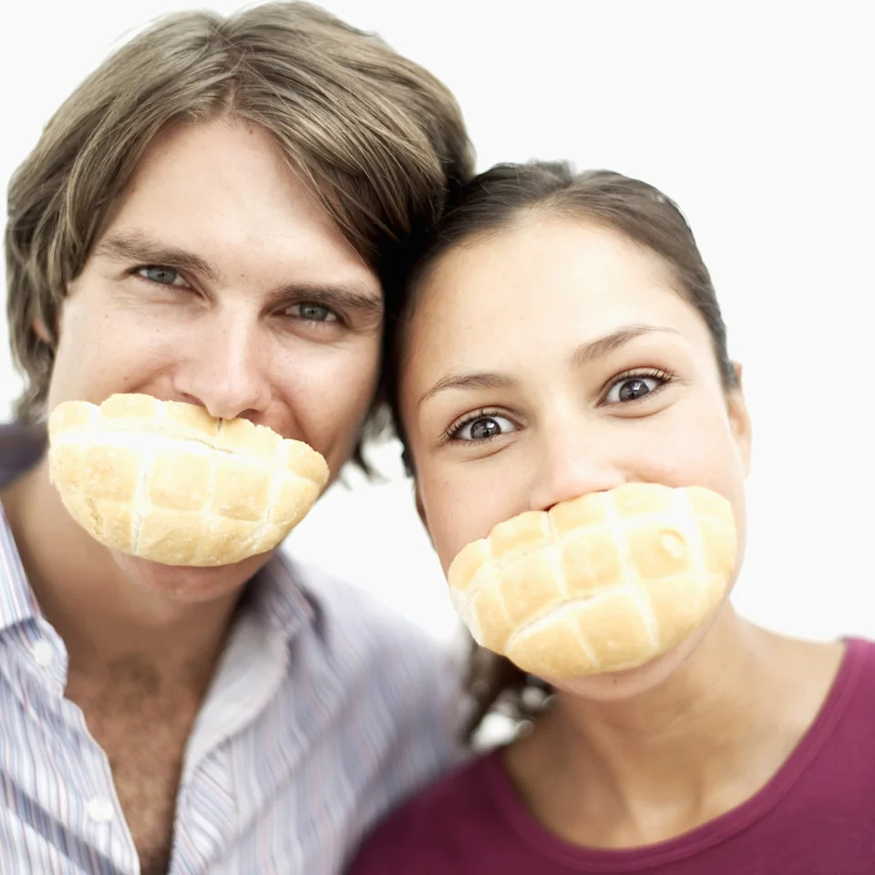 Two people smiling with bread pieces covering their mouths, suggesting playfulness in a romantic context