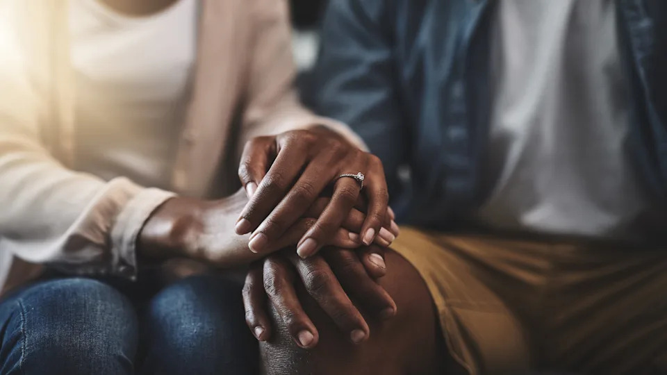 A couple holds hands closely, symbolizing intimacy and connection, with the focus on their interlocked fingers and an engagement ring