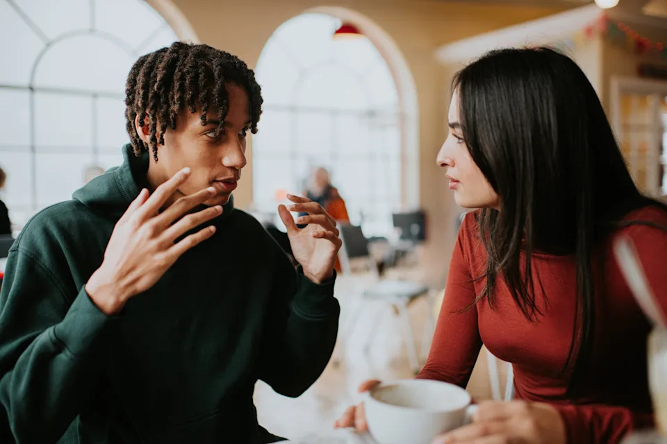 Two people engaged in a deep conversation at a cafe, one gesturing expressively, both appearing focused and connected