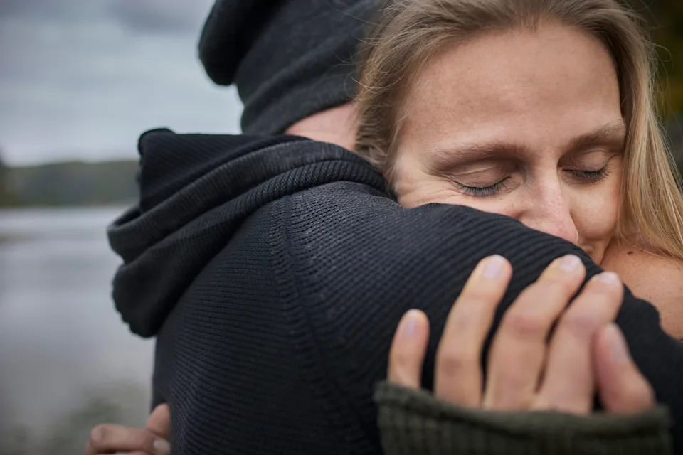 A couple embraces warmly near a serene water backdrop, conveying affection and intimacy