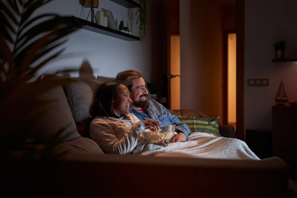 A couple snuggled on a couch, watching TV and sharing a bowl of popcorn in a cozy living room setting