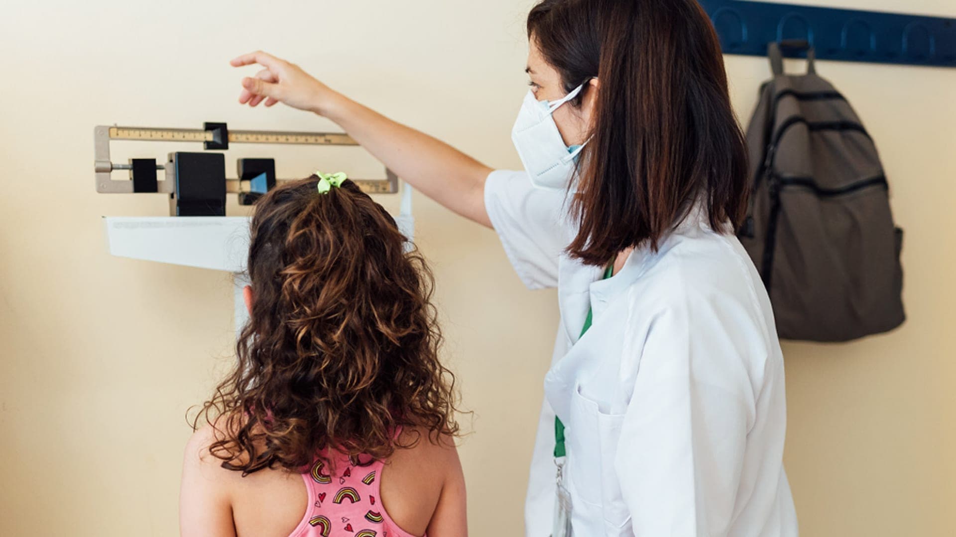 A healthcare professional measures a young girl’s weight during a routine health examination.